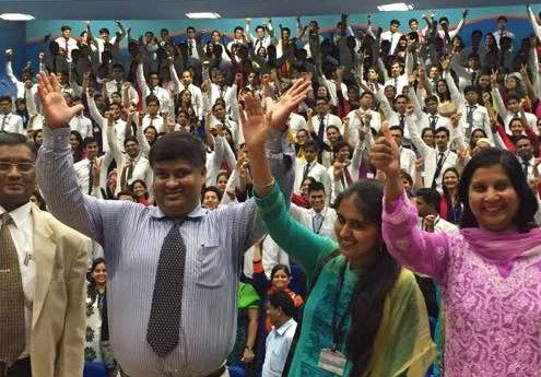 Asif waving for a photograph after delivering a lecture with students in the background.