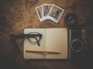 A toned picture with a planner, pencil, photographs, spectacles and a camera placed on a laid out map indicating planning a journey.