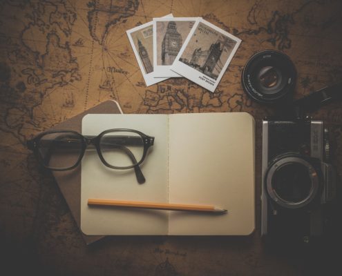 A toned picture with a planner, pencil, photographs, spectacles and a camera placed on a laid out map indicating planning a journey.