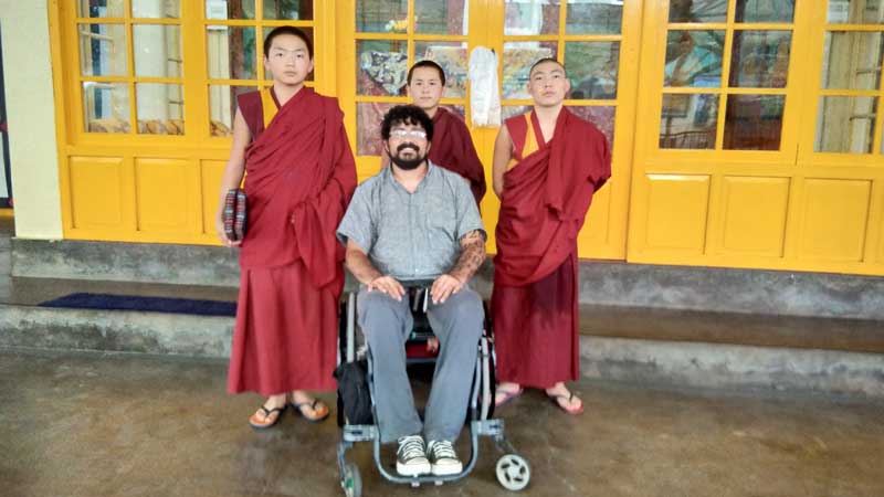 A wheelchair user traveller with 3 monks standing behind him. The yellow door panel is in the background.