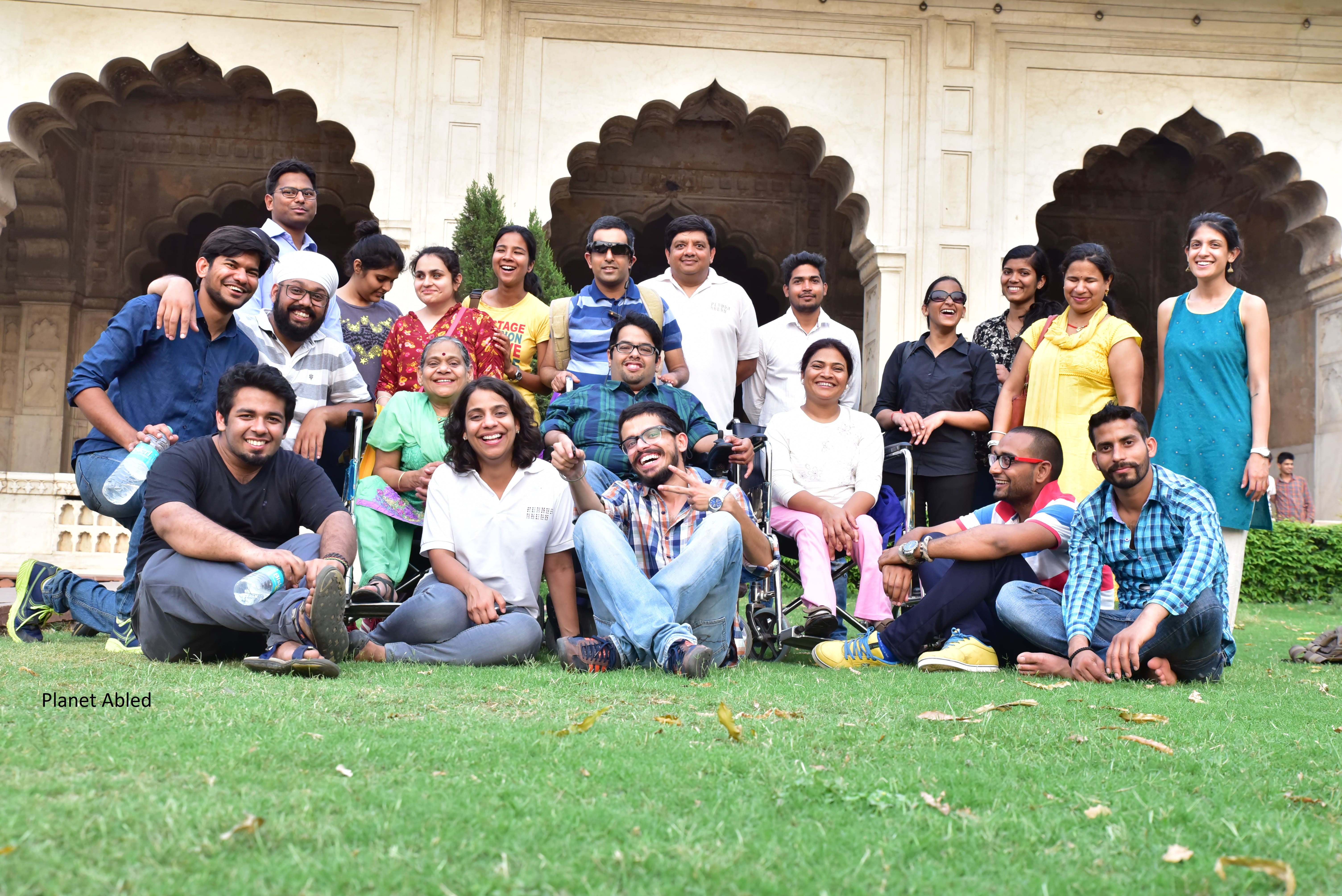 It is a picture of about 20 people with and without disabilities on the premise of a monument. Some are sitting in the grass in front, some in their wheelchairs, and some are standing at the back.